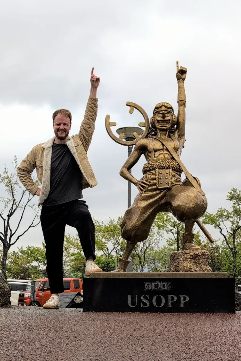 Mann posiert neben Lysop-Statue am Bahnhof Aso in Japan