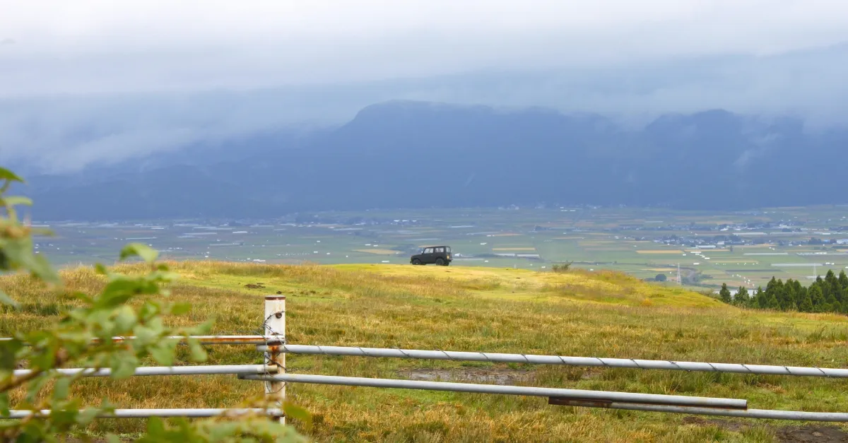 Ein einsamer SUV steht auf einer riesigen Wiese im Aso Grasland