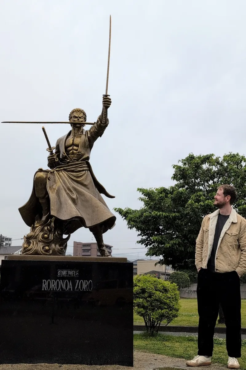 Mann steht neben der Lorenor Zoro-Statue und sieht diese an