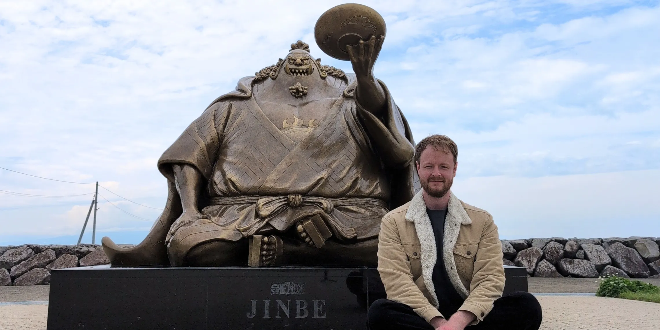 Mann sitzt vor der Jinbei-Statue an der Nagabeta Seabed Road