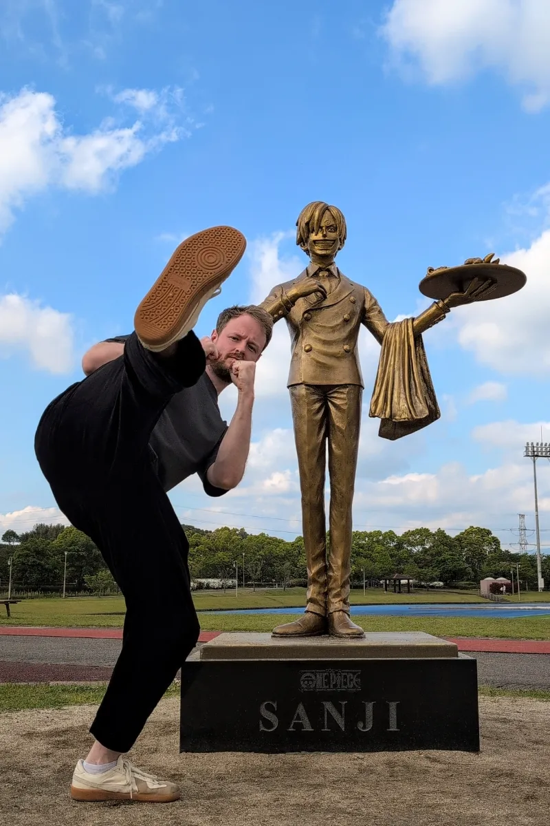 Mann macht neben Sanji-Statue in Mashiki Town eine coole Kick-Pose