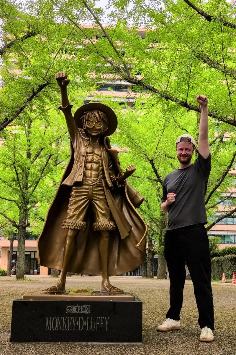 Mann steht neben der Statue von Monkey D. Ruffy in Kumamoto und streckt seinen Arm in die Luft