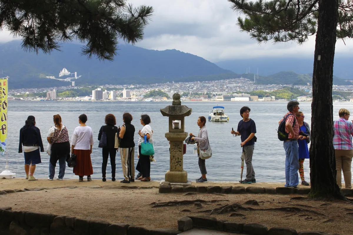 Touristen stehen auf Miyajima in der Nähe des berühmten Torii des Itsukushima-Schreins an, um Fotos zu machen