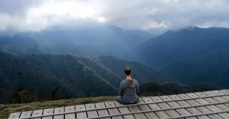 Mann sitzt auf Holzplattform auf dem Gipfel von Mount Tsurugi im Iya Valley und blickt in die Ferne