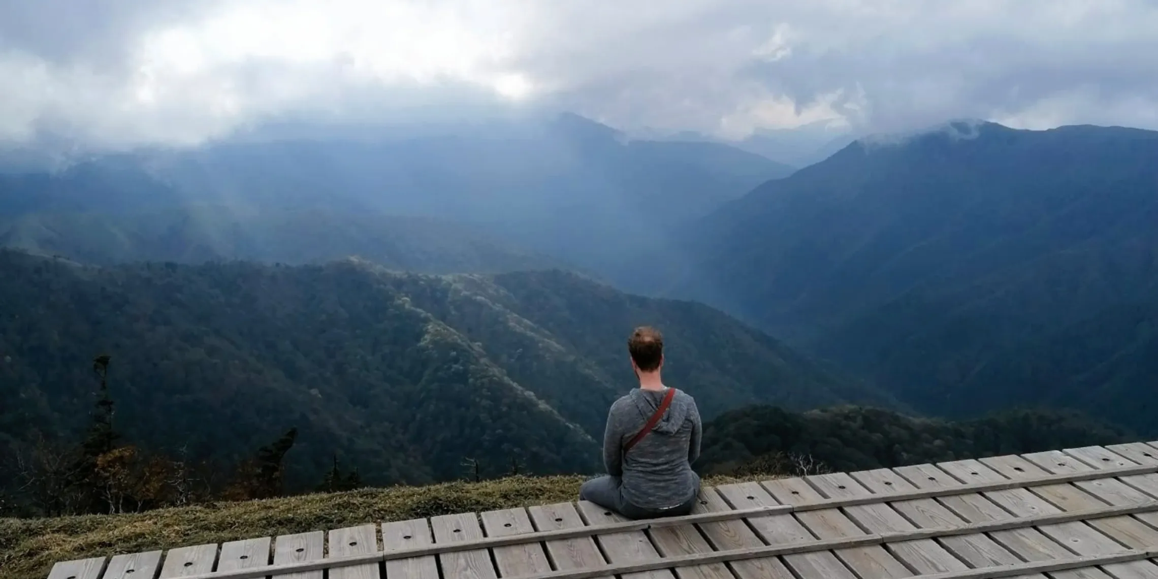 Mann sitzt auf Holzplattform auf dem Gipfel von Mount Tsurugi im Iya Valley und blickt in die Ferne