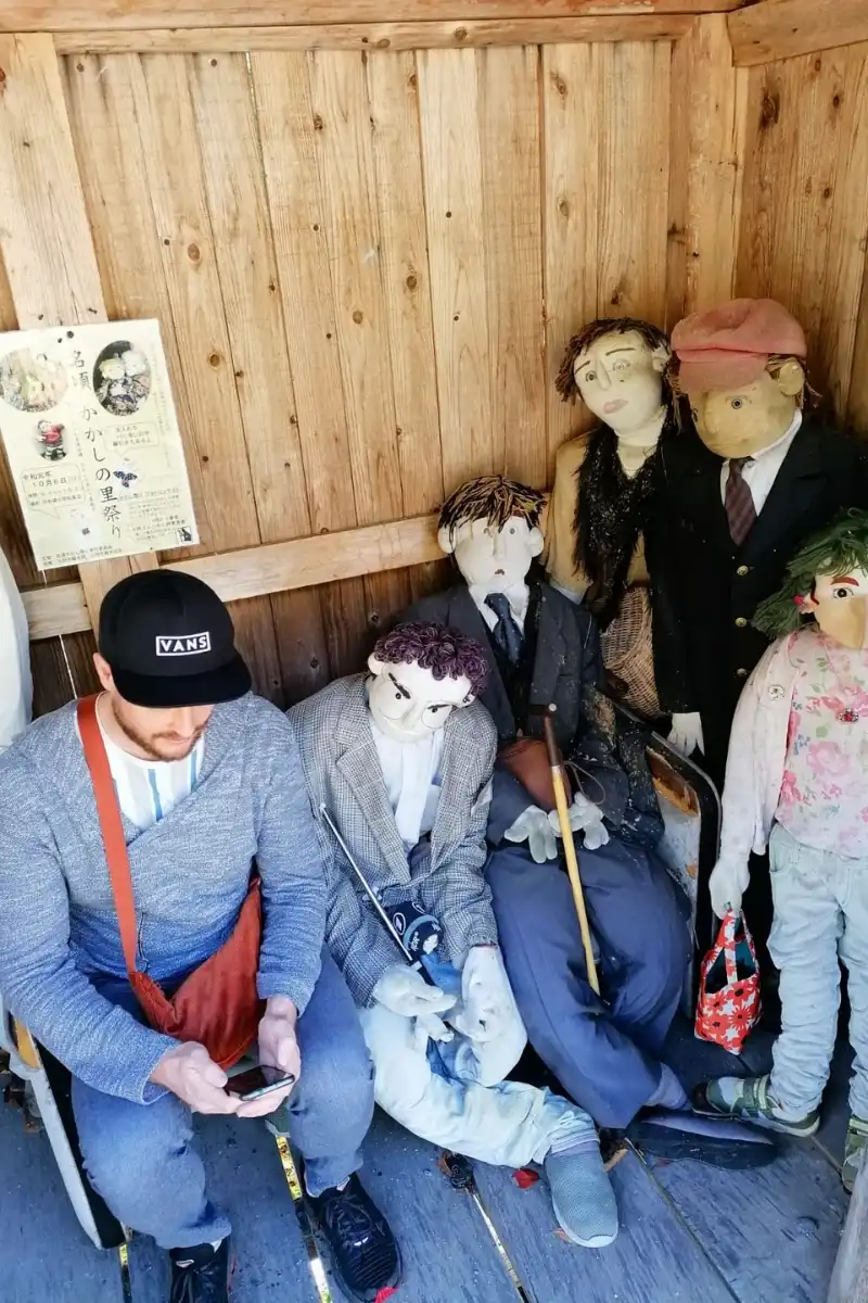 Ein Mann hat sich unter Vogelscheuchen gemischt, die im Nagoro Village an einer Bushaltestelle warten